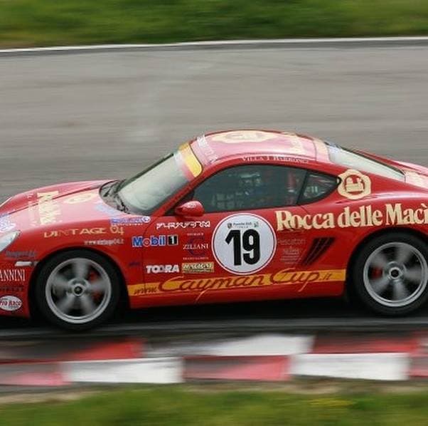 Auto da corsa rossa su un circuito, in movimento veloce, con sticker di sponsor e numero 19 visibile.